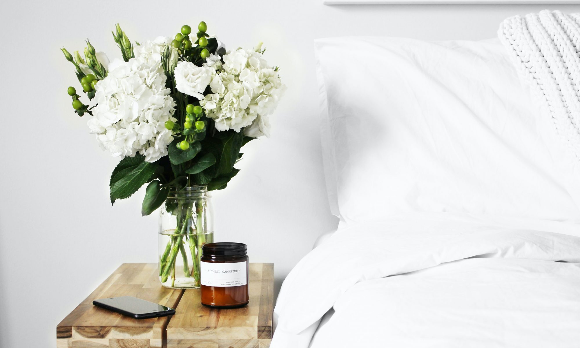 Photo of a bed with white linen, vase sitting on a table next to it
