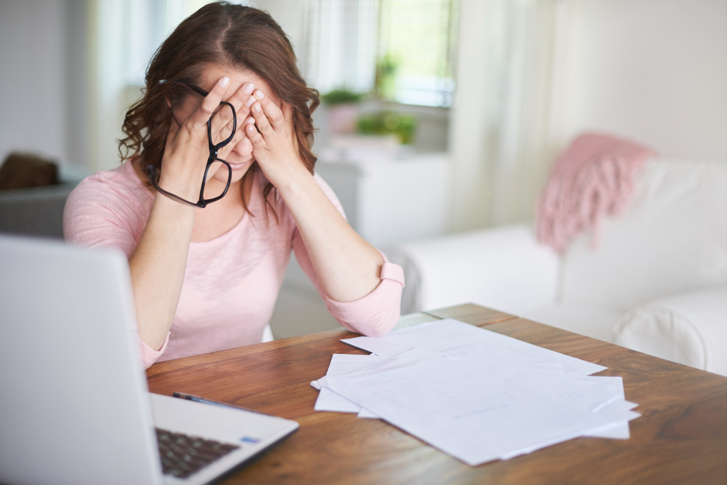 Woman sits at desk with head in hands, stressed over financial pressures