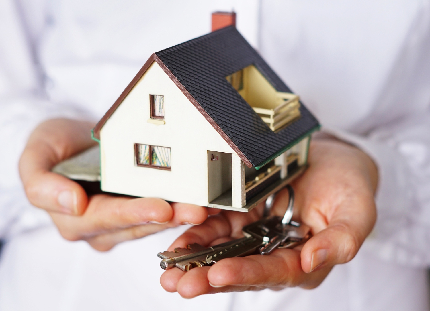 Close up shot of a mini model house and keys in someone's hands