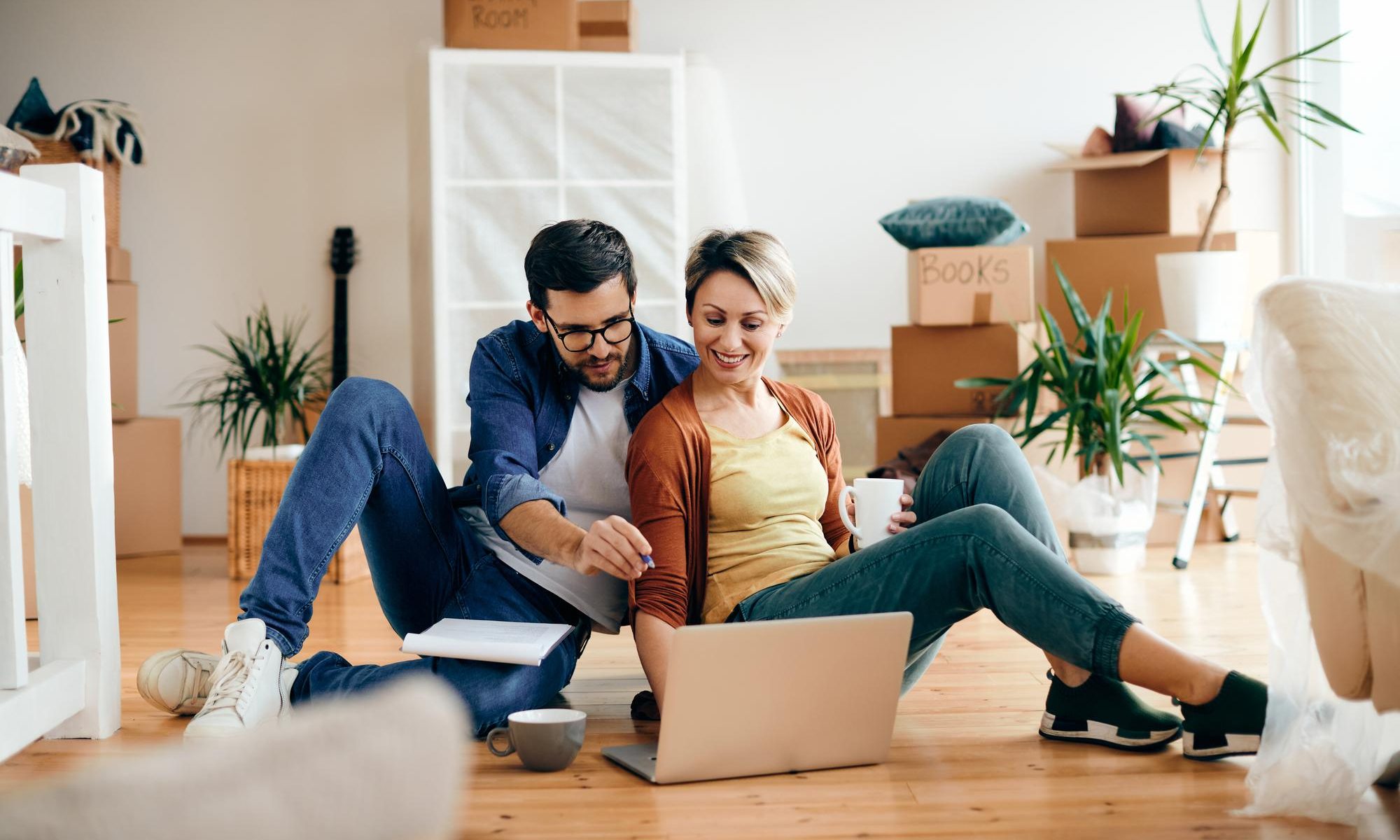 Happy couple relax around a laptop on the floor of their new home