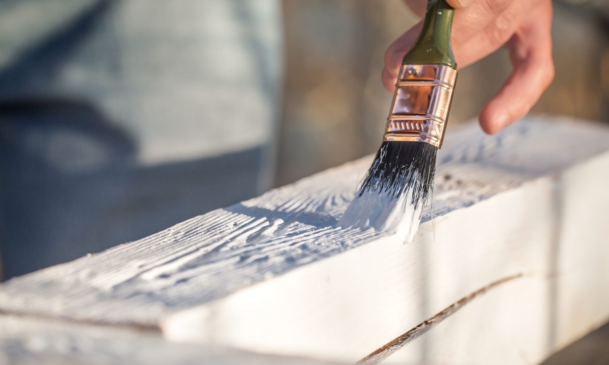 A male hand paints a plank of wood white - painting is a cheap renovation option to increase the value of an investment property
