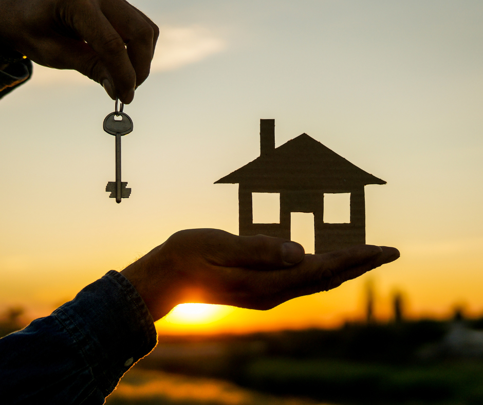 Hands holding a house shape and keys against a sunrise