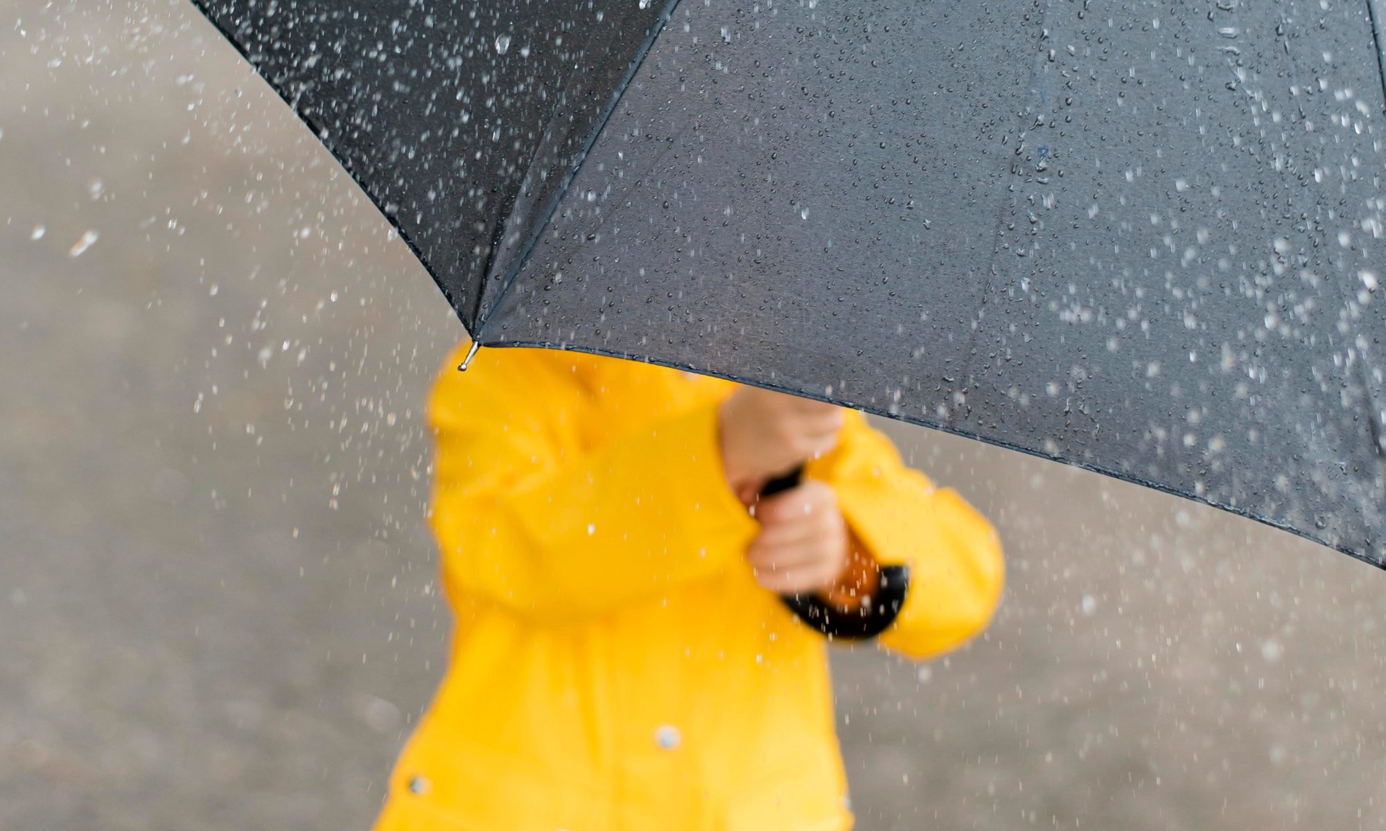 Little child holding big black umbrella in the rain